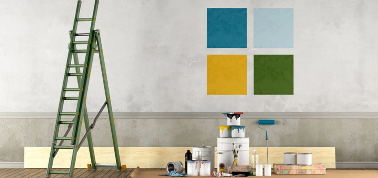 Dispersionen - Malerwerkzeug inklusive verschiedener Farbeimer und Leiter stehen vor einer Wand auf der 4 farblich unterschiedliche Rechtecke gemalt sind.